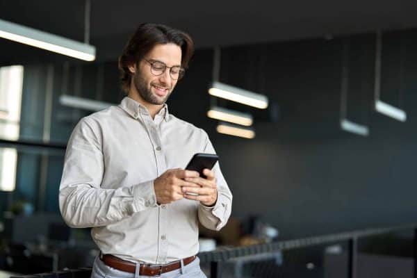 Giovane professionista in un ufficio moderno che usa uno smartphone, rappresentando i motivi per l'adesione al Fondo Telemaco per gli Under 30.