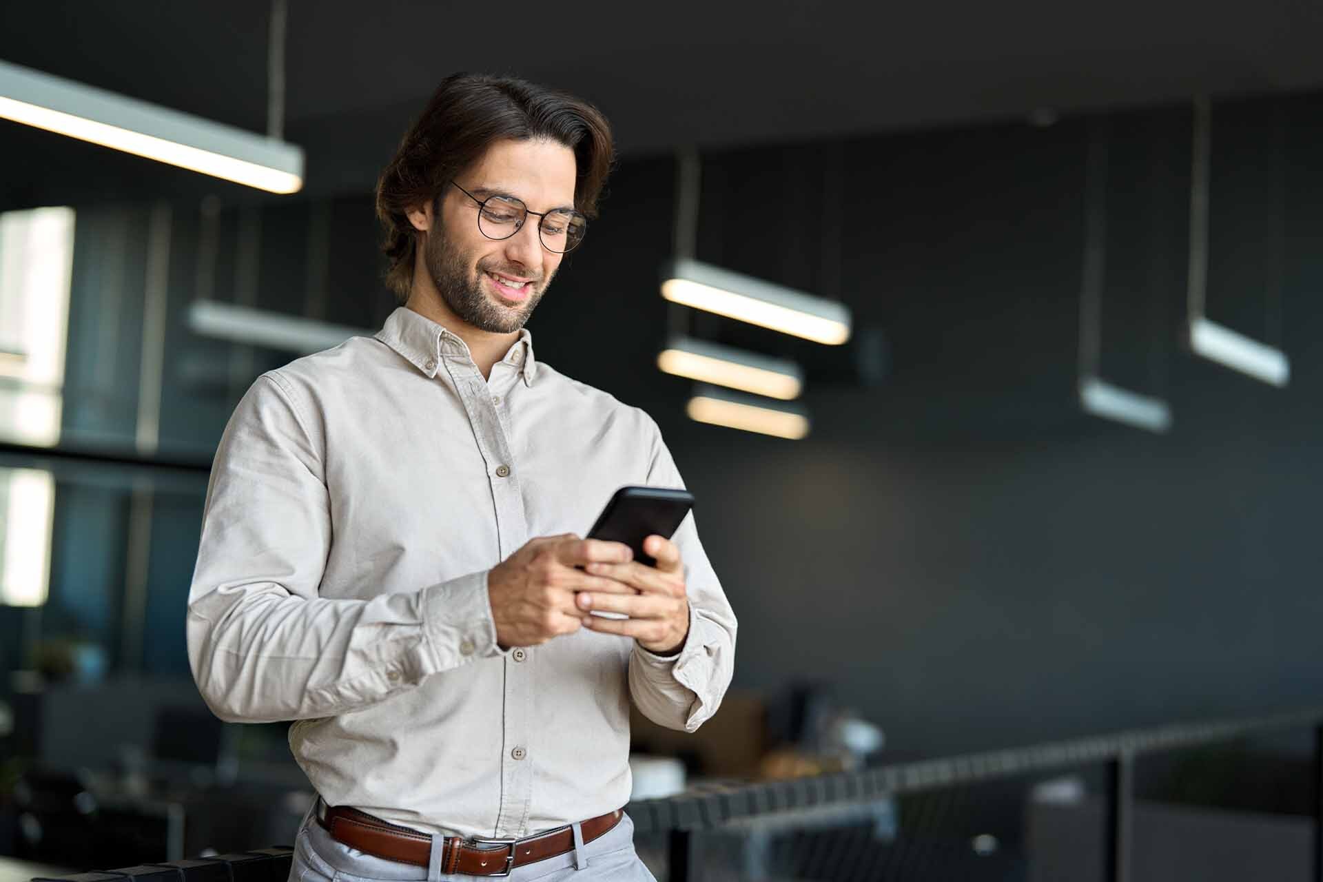 Giovane professionista in un ufficio moderno che usa uno smartphone, rappresentando i motivi per l'adesione al Fondo Telemaco per gli Under 30.