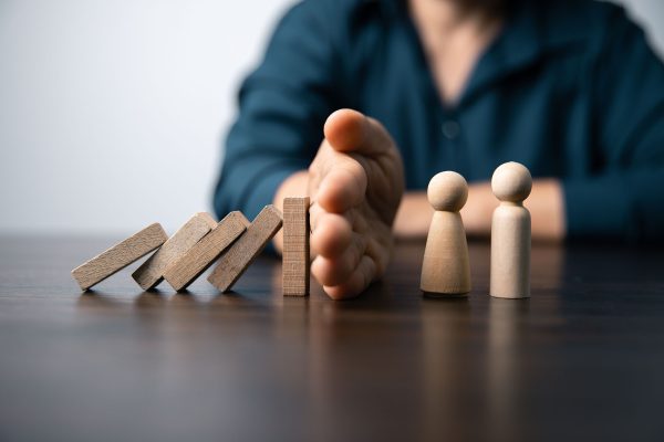Una mano che ferma l'effetto domino per proteggere due pedine di legno, simboleggiando la gestione degli imprevisti finanziari