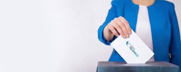 Una persona che indossa una giacca blu inserisce una busta bianca elettorale, riportante il logo del Fondo Telemaco, all'interno di un'urna.