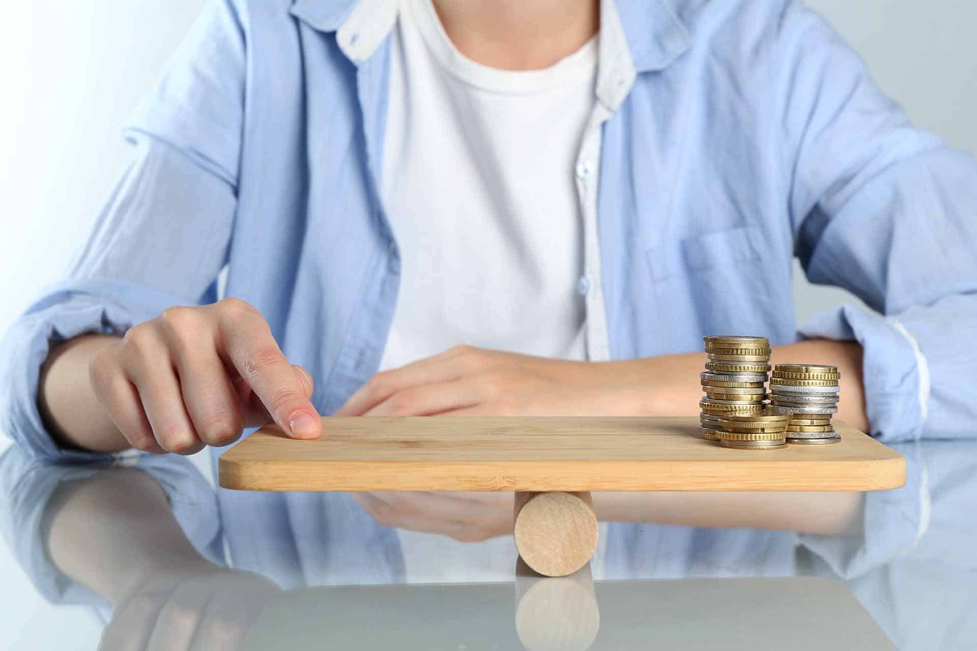 Un esempio visivo dei costi più bassi per i fondi pensione negoziali: una persona bilancia monete su una tavoletta di legno.