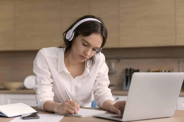 Una giovane donna studia al computer prendendo appunti, simbolo dell'educazione previdenziale come miglior investimento per la pensione.