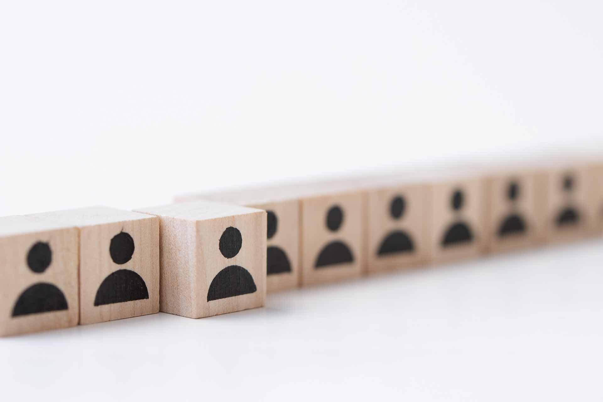 Cubi di legno con icone di persone allineate, con un cubo che si distingue dagli altri, a rappresentare la differenza tra un cliente e un associato nei fondi pensione negoziali.