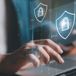 Un primo piano delle mani di una persona che digita su un computer portatile, con icone olografiche fluttuanti di scudi di sicurezza digitali contenenti lucchetti, e flussi di codice binario sfocato sullo sfondo.