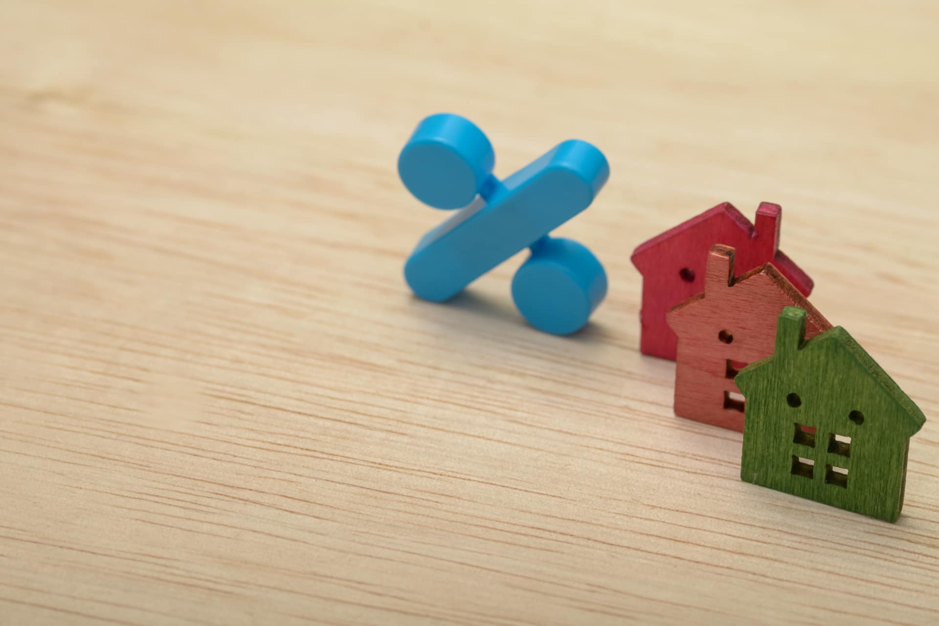Piccole sagome in legno a forma di case colorate e un simbolo di percentuale blu su un tavolo in legno