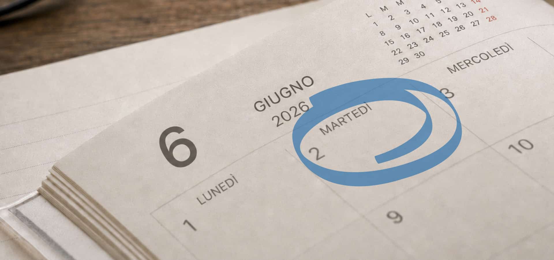 Calendario da tavolo cartaceo aperto sul mese di giugno 2026, con il giorno martedì 2 giugno cerchiato in blu per evidenziare la data.