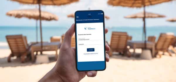 Una mano tiene uno smartphone che visualizza la schermata di login dell'App del Fondo Telemaco. Lo sfondo è una spiaggia sfocata con ombrelloni e il mare.