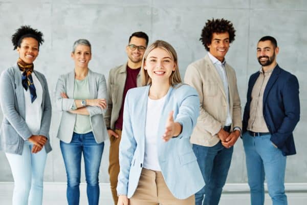 Gruppo di professionisti sorridenti con una donna in primo piano che tende la mano, immagine sulla crescita delle adesioni ai fondi pensione negoziali